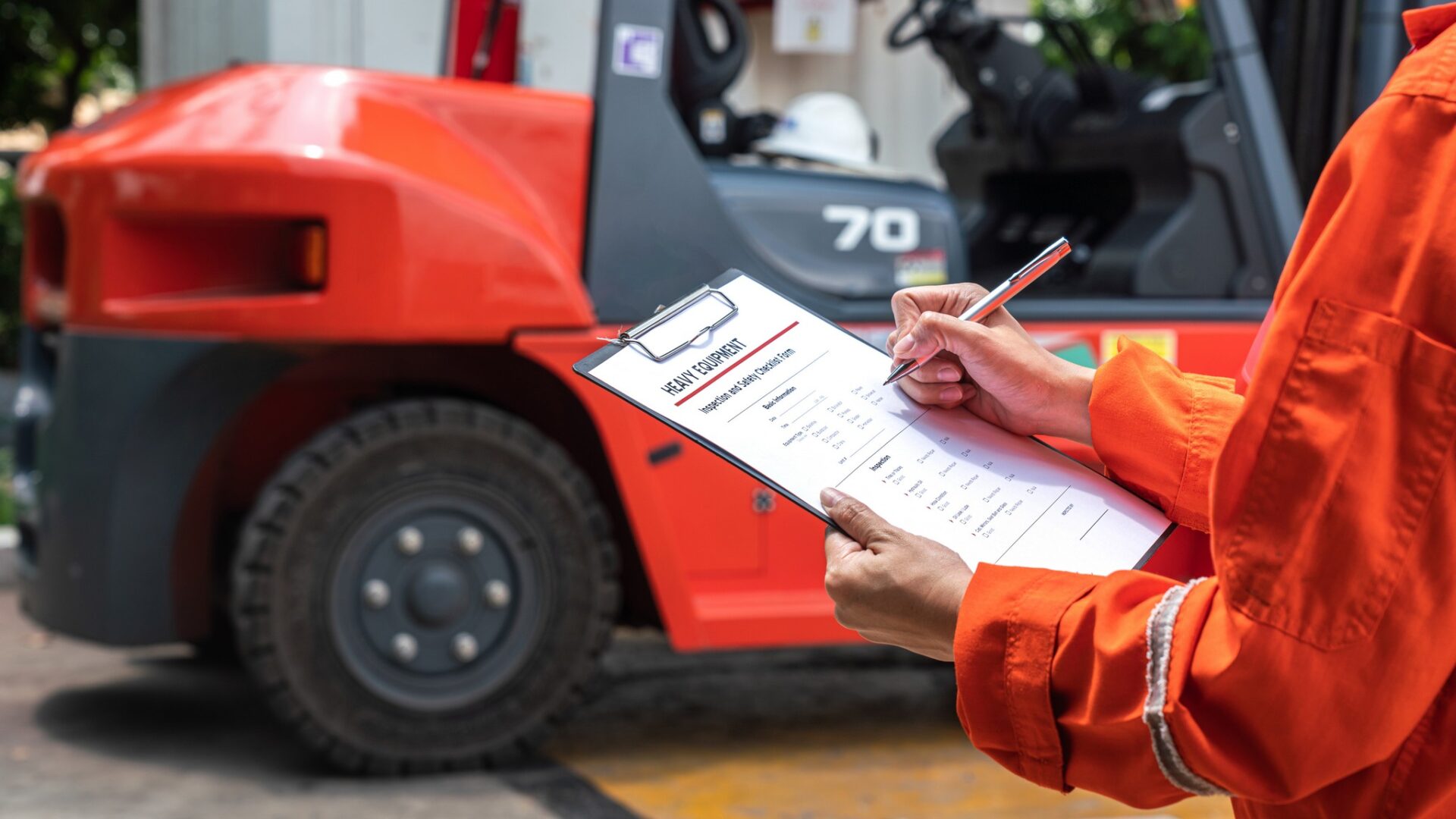 A mechanical engineer is using heavy equipment checklist form for inspecting the factory forklift vehicle (as blurred background). Industrial working with safety practice concept, selective focus.